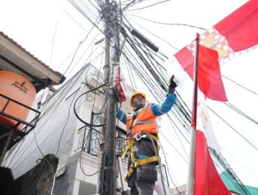 Salah seorang petugas PLN sedang merapikan bendera yang mengenai kabel listrik. (Foto : PLN Jakarta Raya)